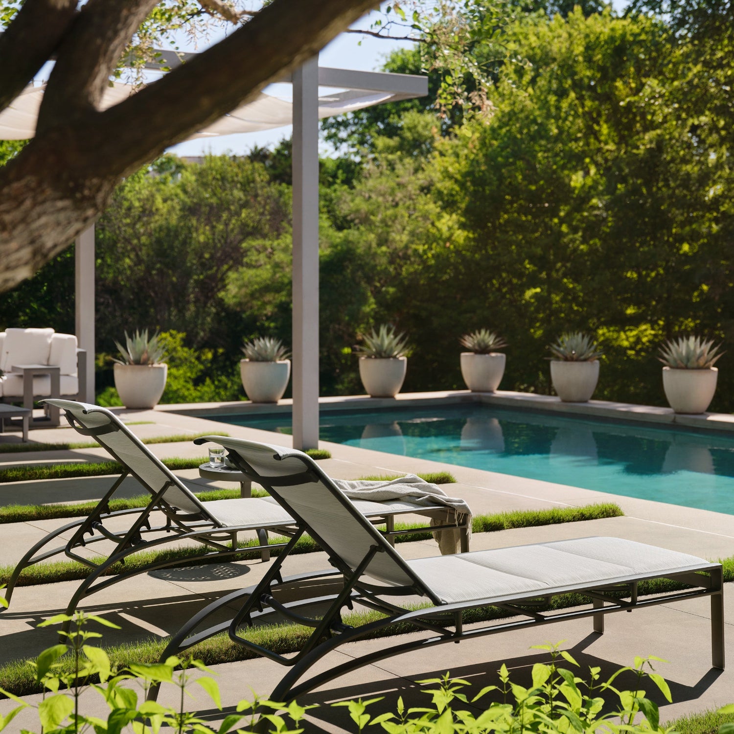 Outdoor pool area with lounge chairs, table, and potted plants.