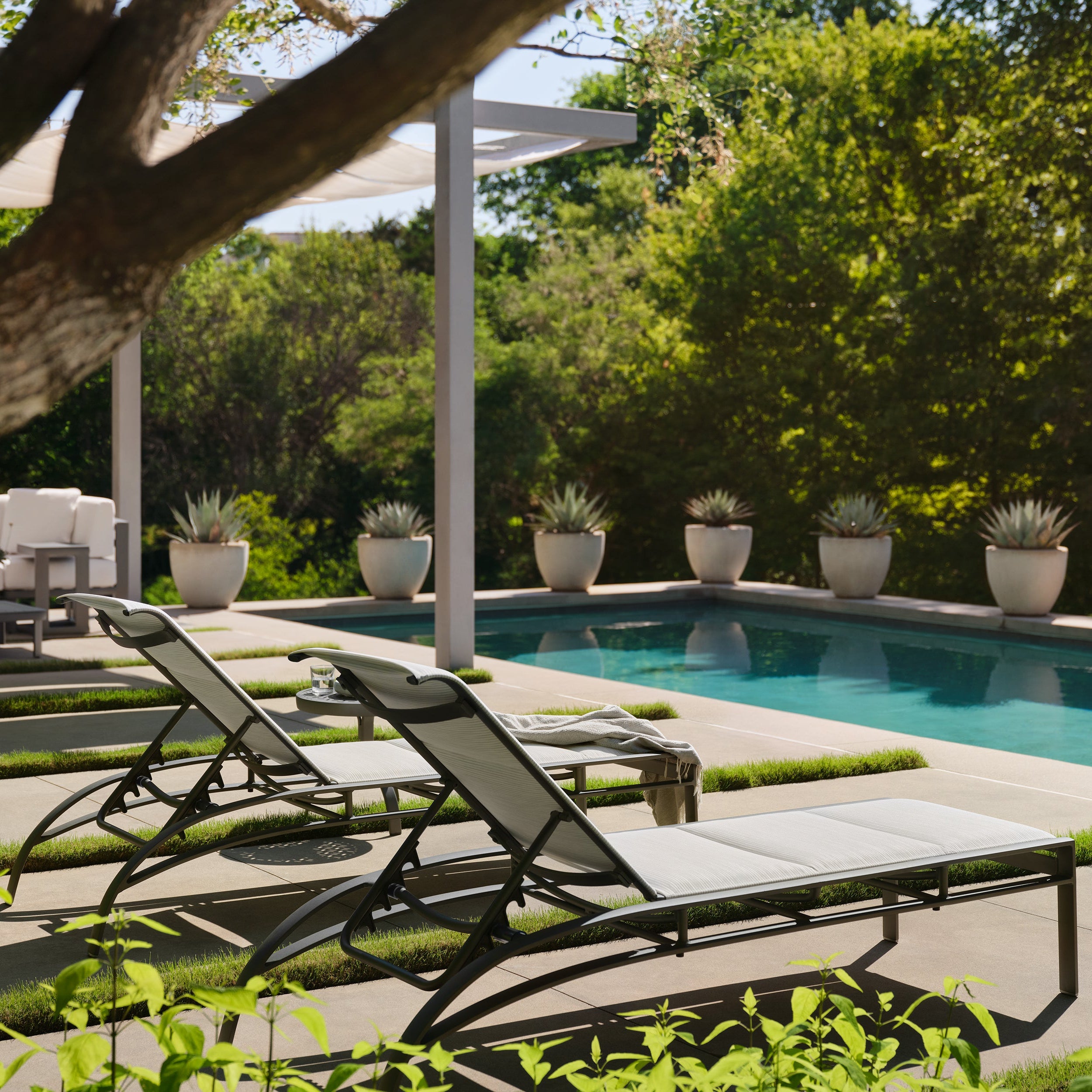 Outdoor pool area with lounge chairs, table, and potted plants.