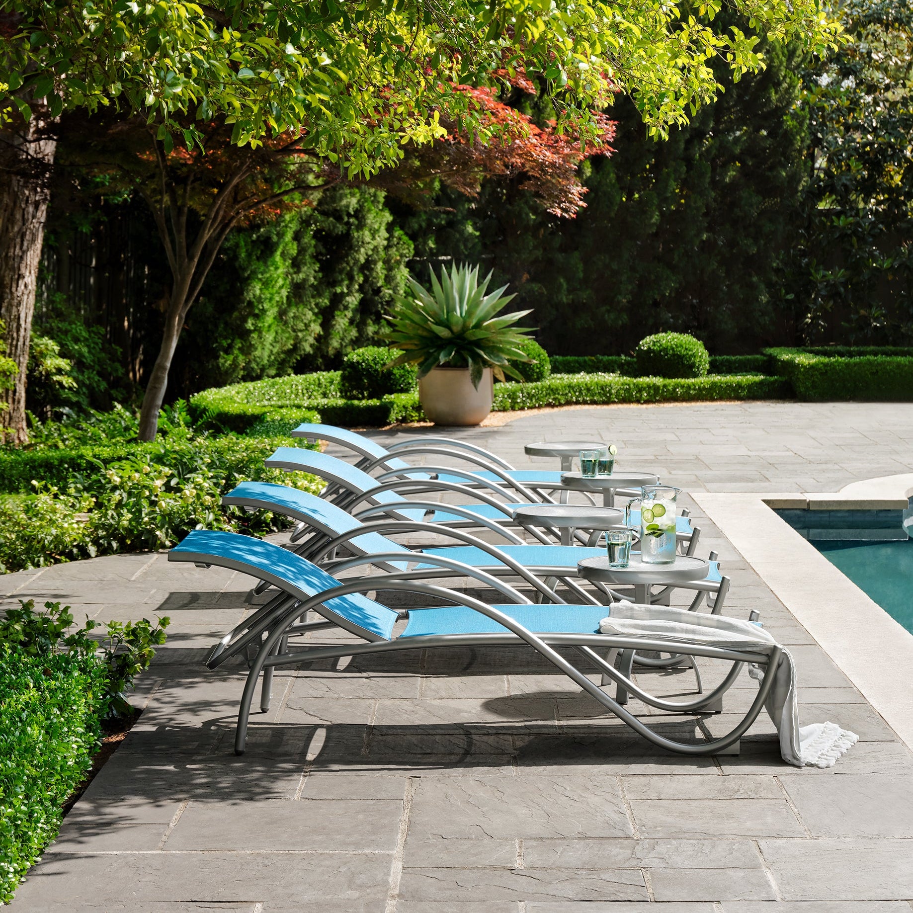 Blue lounge chairs by a pool with greenery in the background