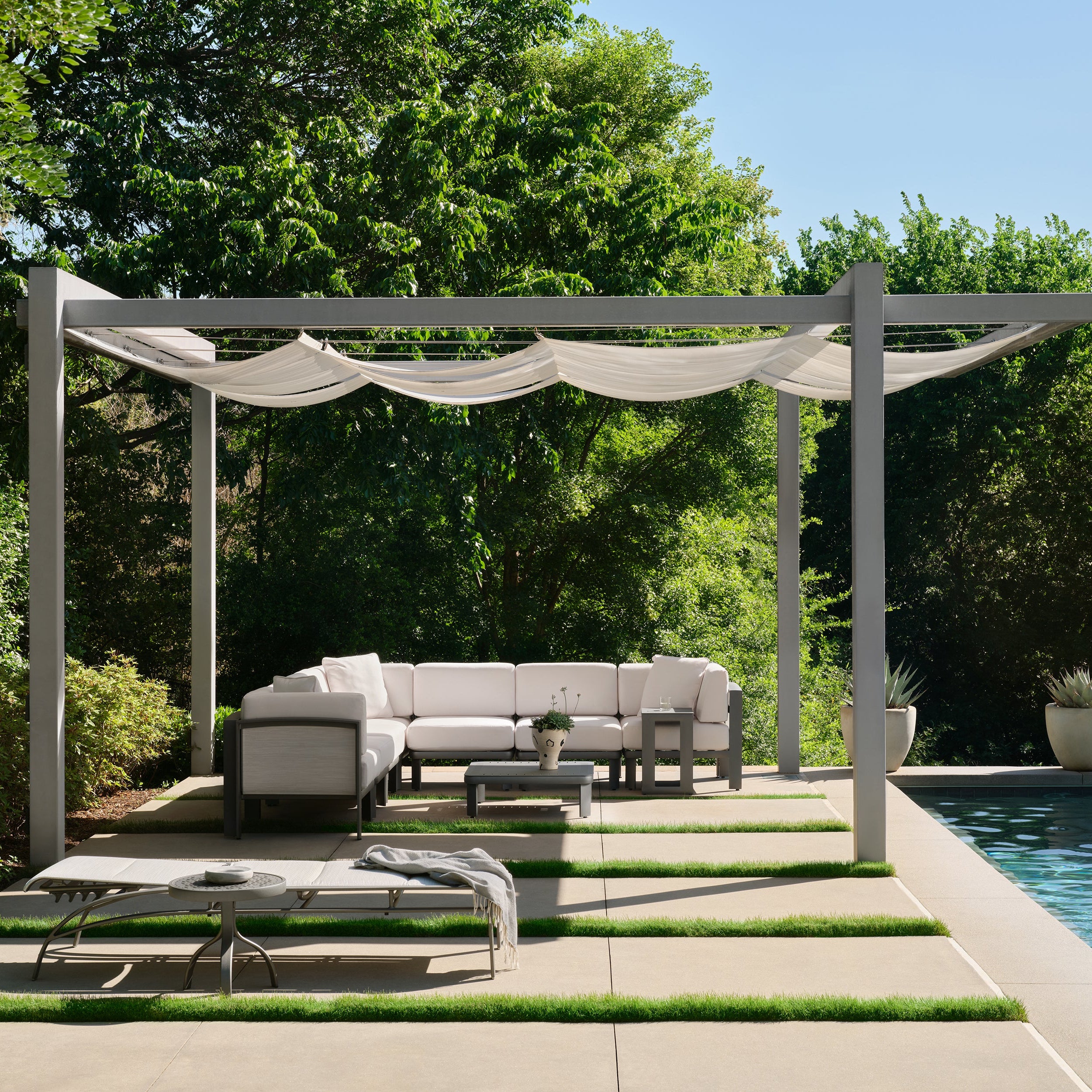 Outdoor patio with pergola, lounge chairs, and sectional sofa by a pool.