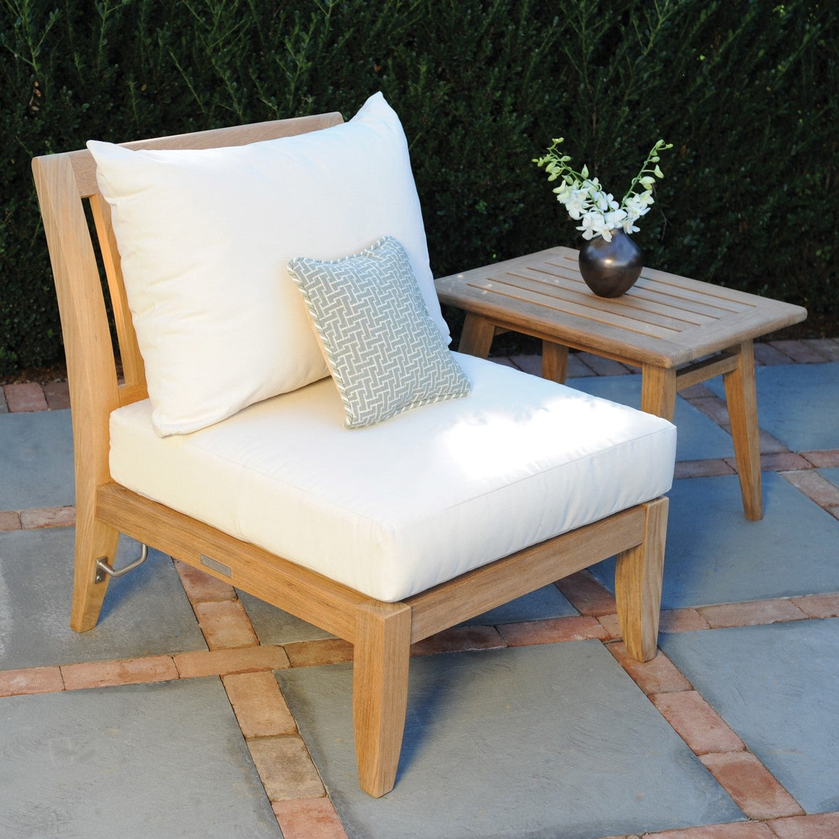 Kingsley Bate Ipanema teak sectional armless chair beside a side table on a patio